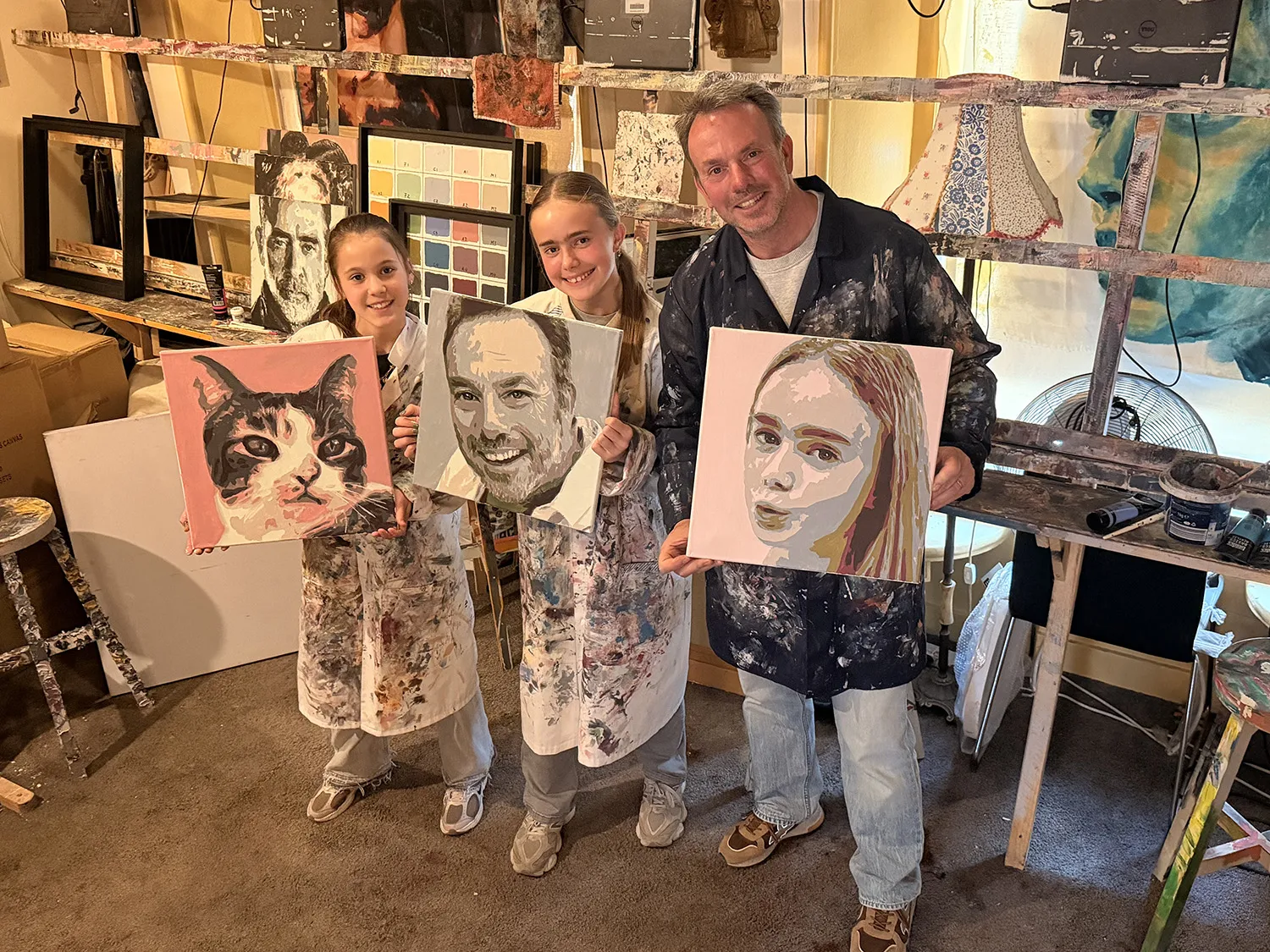 Deelnemers tonen hun zelfgeschilderde portretten in het atelier, waaronder een kat
