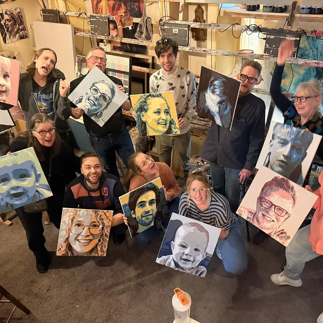 Enthousiaste groep van een bedrijfsuitje toont hun zelfgeschilderde portretten in het atelier